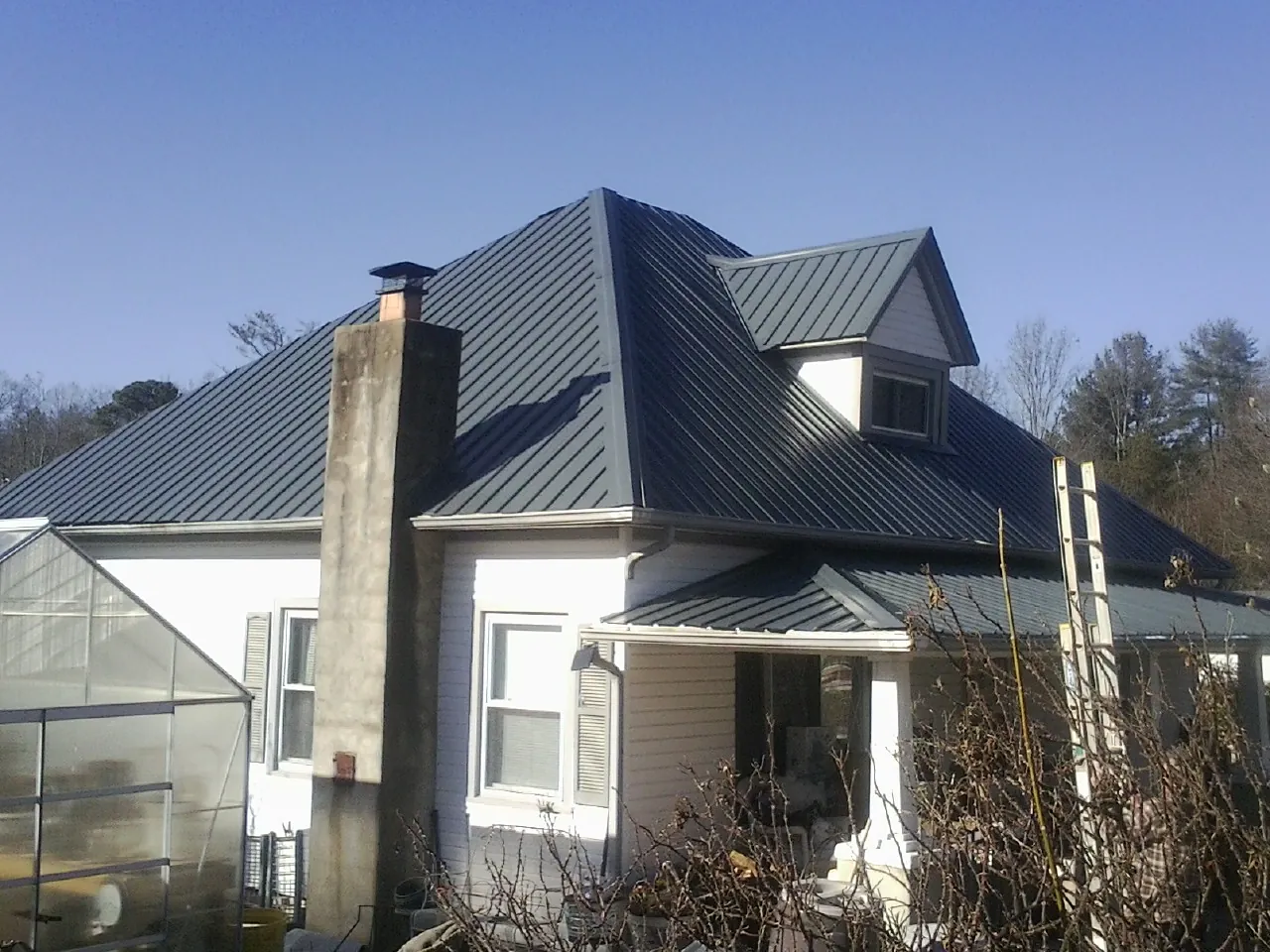 Dark blue standing seam metal roof on a white farmhouse with dormer — Slate & Tile Roof Repair by Roofing Brothers in Belen