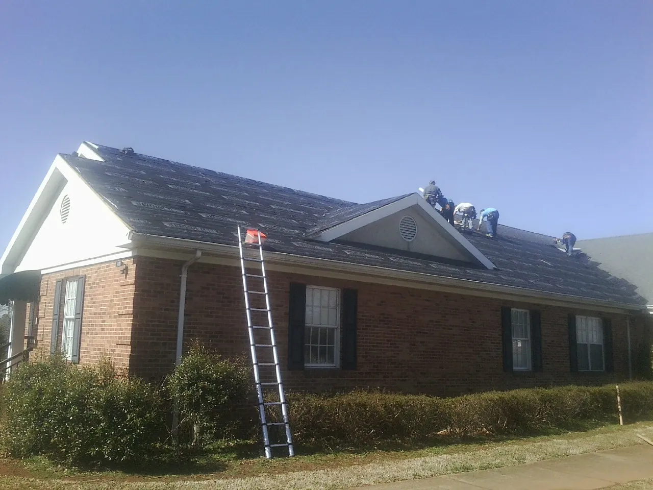 Crew tearing shingles off a brick ranch roof with a ladder set — Metal Roof Repair work by our crew in Belen