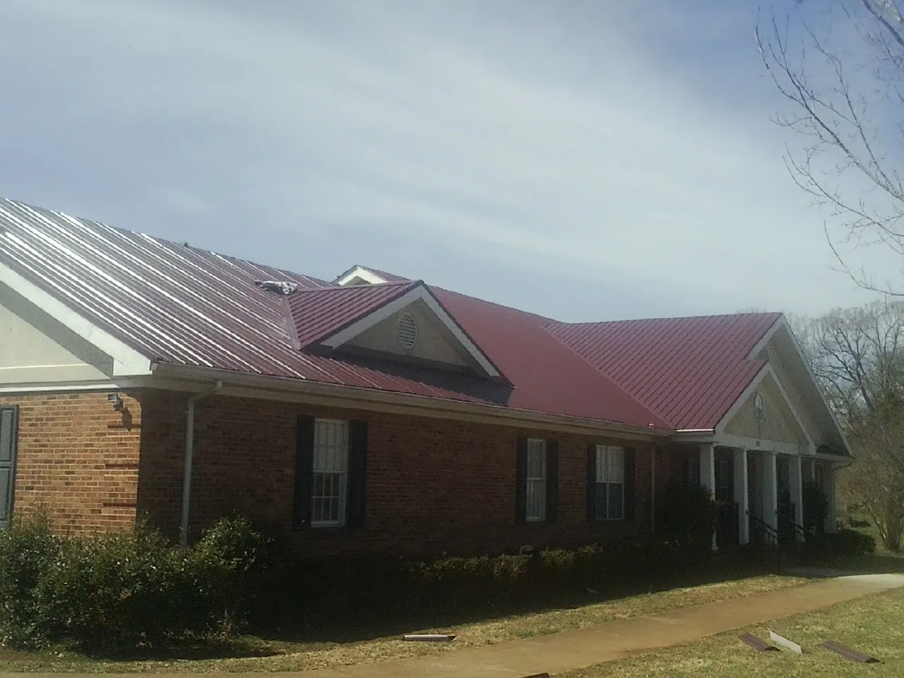 Red metal roof with gabled entries on a long brick building, from a Hail Damage Roof Repair job in Belen