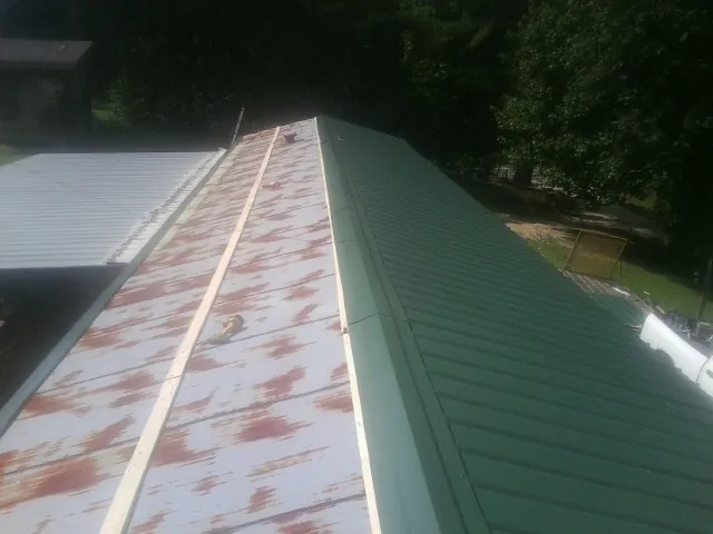 Old rusted panels beside newly installed green metal roofing — Wind Damage Roof Repair by Roofing Brothers in Belen
