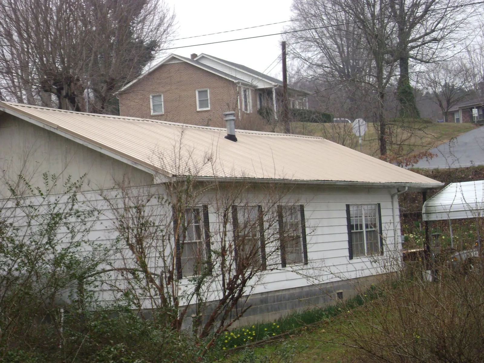 Tan metal roof on a white sided house set into a hillside — Commercial Roofing by Roofing Brothers in Belen